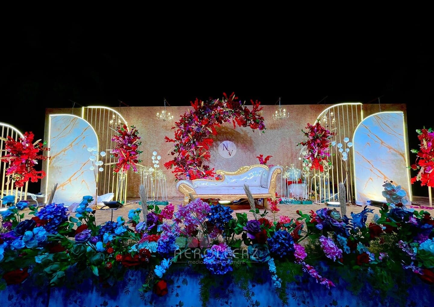 A reception stage framed by a floral arch and layered seasonal blooms